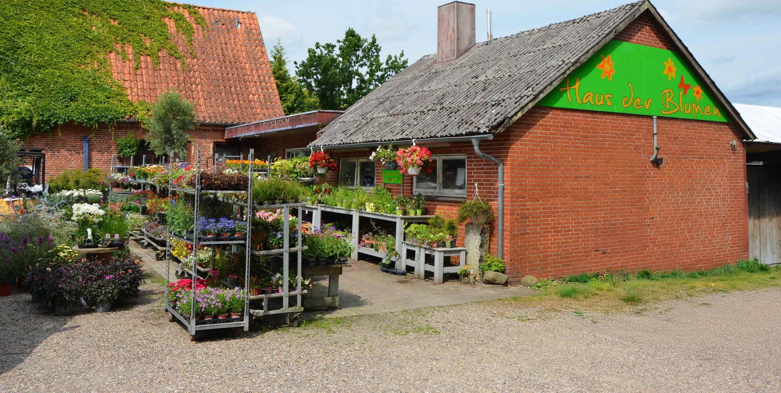 Rotes Backsteingebäude mit grünem Schild "Haus der Blumen" und Blumenverkaufsfläche